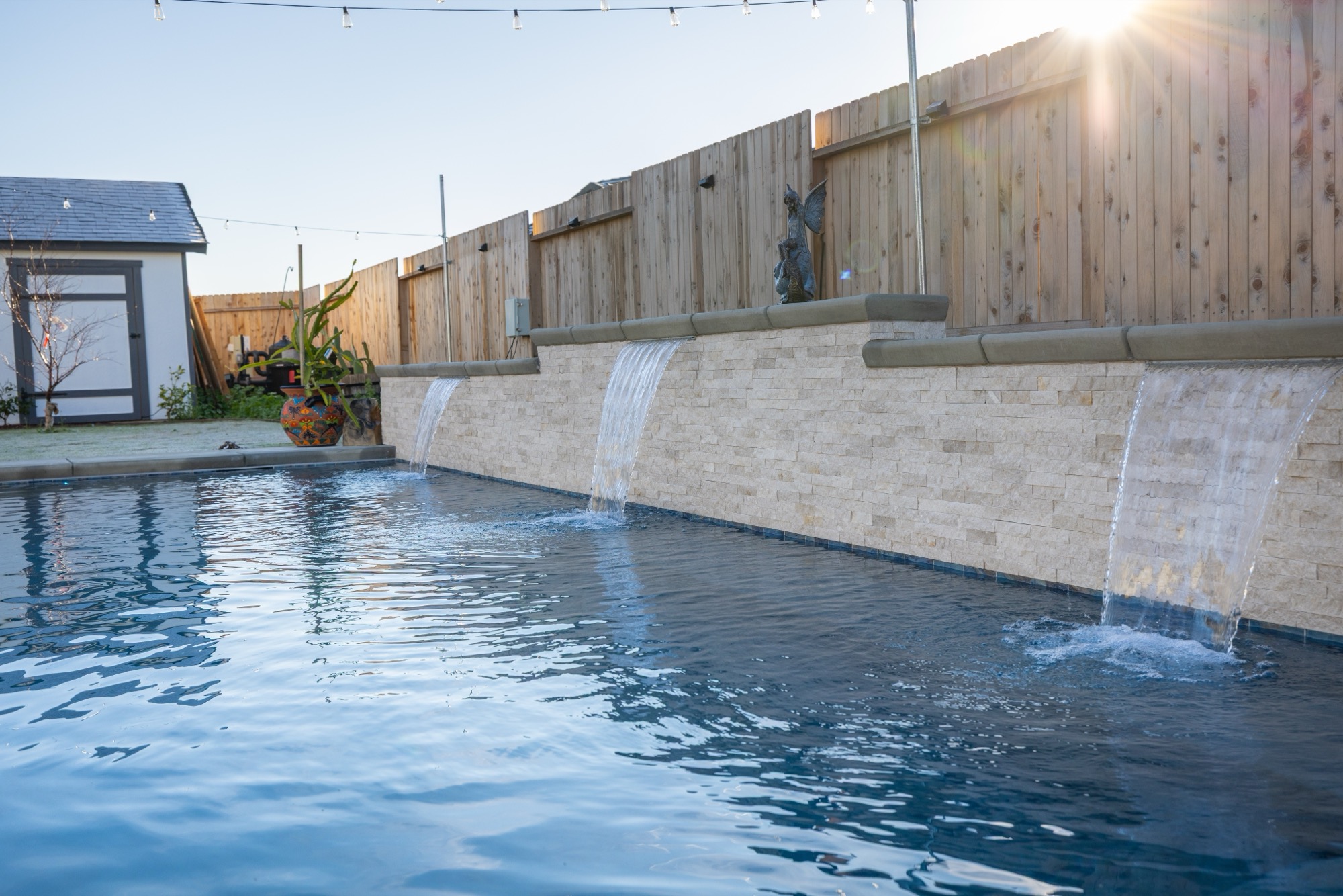 Custom gunite pool with dark plaster and waterfalls at golden hour — Bakersfield, CA